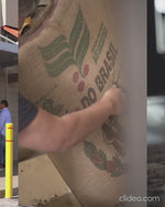 Load and play video in Gallery viewer, Worker carrying a burlap sack of green coffee beans on one shoulder

