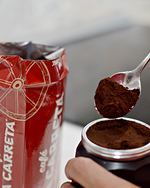 Load image into Gallery viewer, Spoon lifting finely ground Café La Carreta coffee from an opened brick pack into a portafilter
